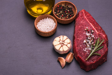 Raw Beef Steak, salt, pepper, garlic, rosemary  on the black board, background.