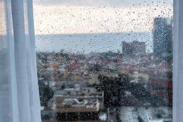 Rain drops over a window with modern city view