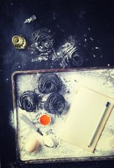 Uncooked black pasta and ingredients for homemade spaghetti Italian food.Notepad to write the prescription.Toned image.Vintage style.Copy space.selective focus