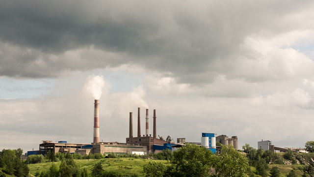 a factory or a plant on the mountain. There is smoke. Floating clouds. Nearby houses