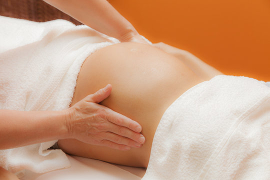 Pregnant young latina woman with beautiful skin, being wrapped with a towel, lying on a bed and having a relaxing prenatal massage, various techniques, glamour clarity effect