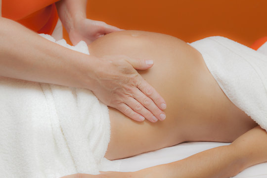 Pregnant young latina woman with beautiful skin, being wrapped with a towel, lying on a bed and having a relaxing prenatal massage, various techniques, glamour clarity effect