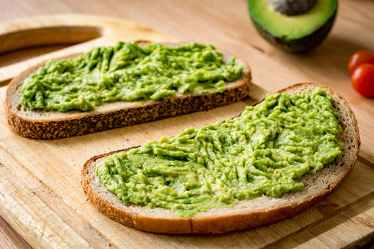 Guacamole and bread. Toast with avocado on wooden cutting board. Warm tone