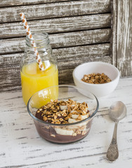 Delicious breakfast or snack - chocolate yogurt with granola and a banana and orange juice.  On light rustic wooden background