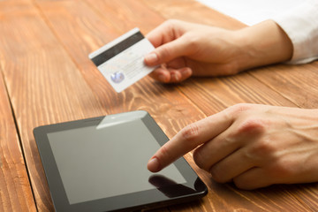 Hands holding credit card typing numbers on tablet pc making online payment at home the wooden table. Online shopping concept. Selective focus.