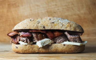 Pork tenderlion sandwich with bacon and blue cheese on wooden background with softlight