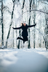 Girl Wearing Warm Winter Clothes And Hat Blowing Snow outdors in the forest and jump