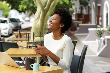 Young african woman laughing with mobile phone at cafe