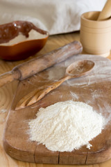 a handful of flour and a wooden spoon on a chopping board and rolling pin with a mortar and pestle on the table. Rural bakery concept, selective focus