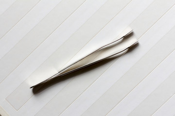 philatelic tweezer made of stainless steel on a blank page for the album of stamps diagonally. top view close-up