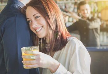 Attractive girl is smiling and drinking cocktail supported by her boyfriend - loving couple-  during a party - caucasian people - love, party, drink and people concept