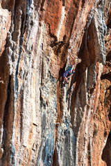 Young Rock Climber ascending steep colorful rocky Wall Lead Climbing