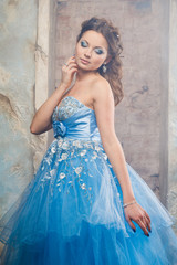 Fototapeta premium Beautiful young woman in gorgeous blue long dress like Cinderella with perfect make-up and hair style
