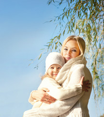 Smiling happy blonde woman and girl hugging outdoor in park against blue sky.