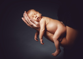 newborn baby sleeping in the hands of his father on a dark