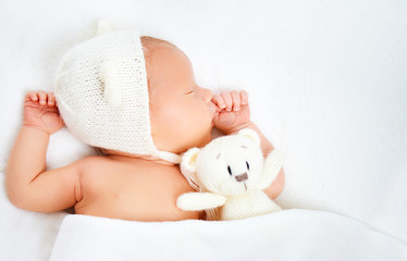 Cute newborn baby in bear hat sleeps with toy teddy bear