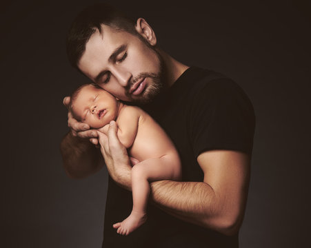 newborn baby sleeping in his arms of father on dark
