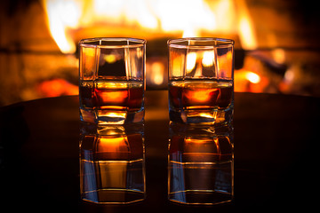 Two glasses of alcoholic drink in front of warm fireplace. Magical relaxed cozy atmosphere near ...