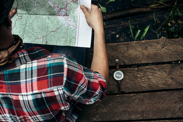 stylish hipster traveler exploring map at sunny forest and lake