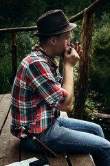 stylish hipster traveler playing harmonica at sunny lake in the