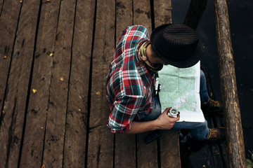 stylish hipster traveler exploring map at sunny forest and lake
