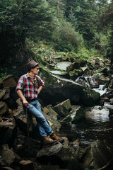 stylish hipster lumberjack with ax in the sunny forest at the ri