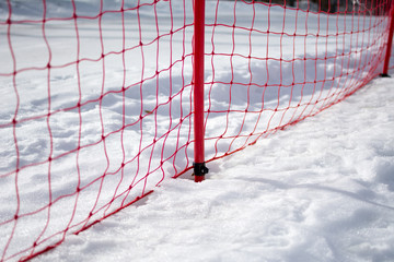 Winter landscape on snow mountain. In focus is security fence, close to the ski track where people skiing down the slope