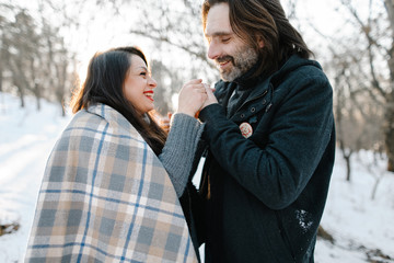 Fototapeta premium Cute young hipster man and pregnant mom having fun in winter park on a sunset hugging each other and smiling 