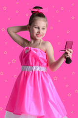Little girl in a bright dress looks in the mirror and doing make