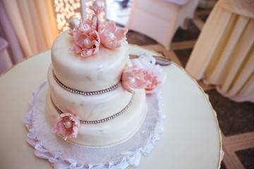 Obraz na płótnie Canvas big sweet multilevel white wedding cake with cream roses on a white table