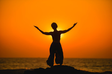 Female meditates during yoga and opens her body to the sun at a sunset