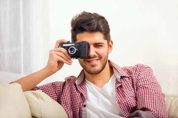 Fototapeta premium Man holding retro camera, sitting on sofa at home