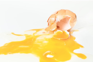 Broken and crushed egg with yolk and egg white on white board, macro