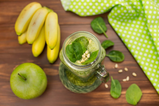 Healthy green smoothie with spinach, green apple, bananas and pine nuts in a jar mug on rustic wooden background from top view. 