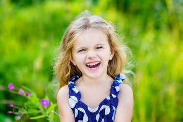 Fanny and beautiful laughing little girl with long blond curly hair in summer park