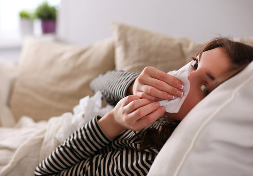 Portrait of a sick woman blowing her nose while sitting on the sofa 
