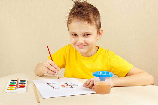 Little boy in a yellow shirt painting with watercolors