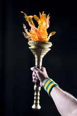 Hand of Brazilian athlete holding sport torch against a black background