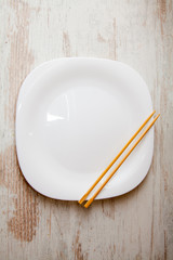various sushi on white plate with chopsticks at wooden background