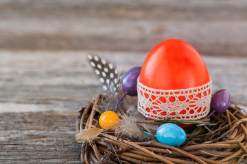 Red Easter egg decorated with lace in small nest on wooden background