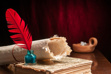 Red quill pen and a rolled papyrus sheet on an old book