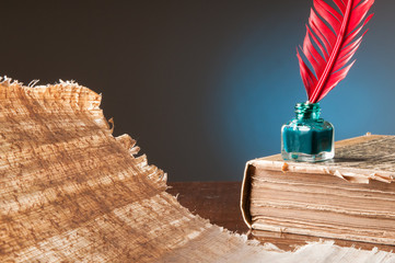 Red quill pen and a papyrus sheet on a wooden table in a blue background