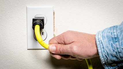 Man plugs an extention cord into a garage outlet - obrazy, fototapety, plakaty