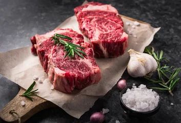 Fotobehang Steakhouse Twee rauw vers gemarmerd vlees black angus steak ribeye, knoflook, zout en op donkere achtergrond