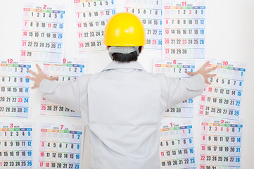 カレンダーを見て考える作業服の男性