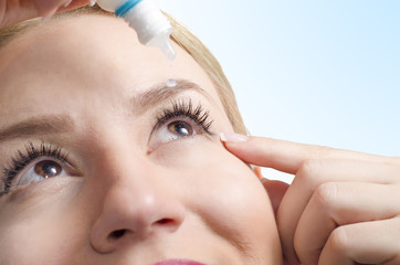 Closeup of young woman applying eye drops, selective focus only on right eye. Drop captured in mid...