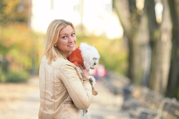 Young woman holding her cute Maltese terrier looking at camera over the shoulder