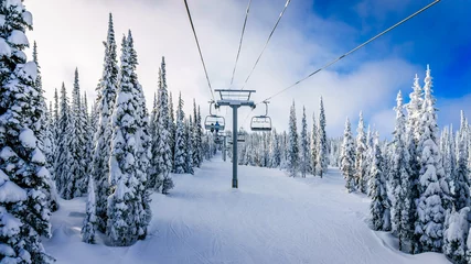 Fototapeten Alpine ski lift and snow covered pistes and trees on a cold winter day under beautiful sky on Mount Morrisey at the village of Sun Peaks in the Shuswap Highlands of central British Columbia © hpbfotos