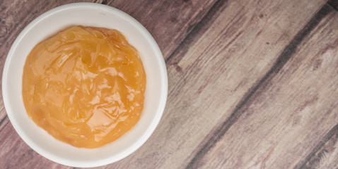 Orange fruit curd in white bowl over wooden background