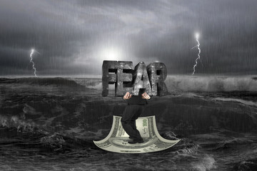Businessman carrying structure of FEAR on money boat with storm